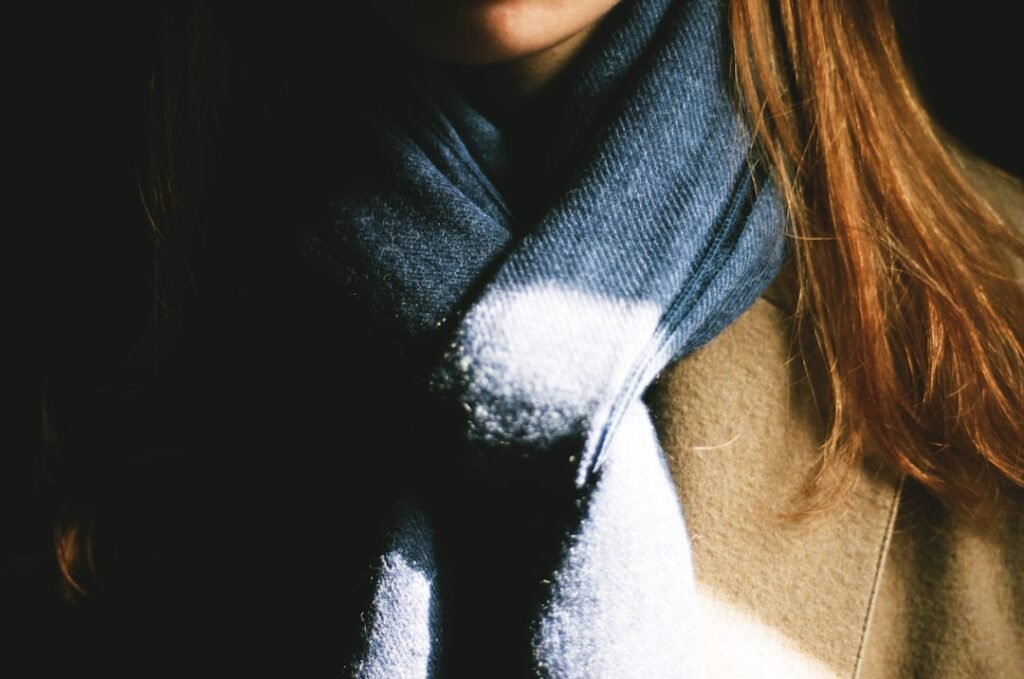 Close-up of a grey and white wool scarf draped over a camel coat collar, showing the texture and layering of a classic winter scarf look.