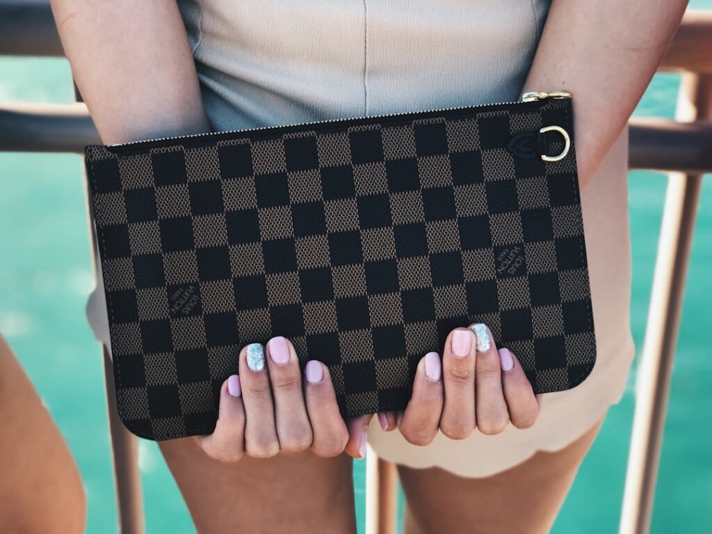 Louis Vuitton Damier canvas clutch held in hands, showing the canvas pattern that buyers should examine when authenticating an LV bag