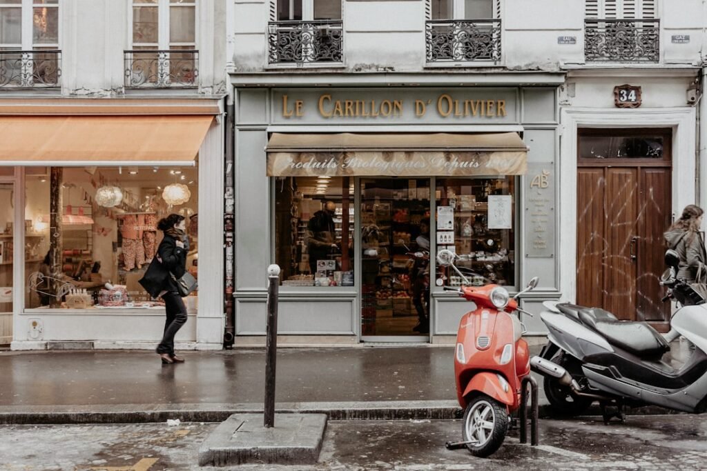 Woman in a dark coat walking past a classic Parisian shopfront on a rainy winter day, illustrating the wet cobblestone streets of Paris in January.