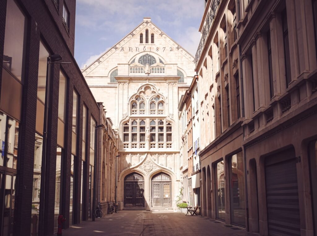 A narrow pedestrian passage in Antwerp, Belgium, with a historic stone church facade at its end, illustrating the intimate, walkable character of the city's fashion district streets