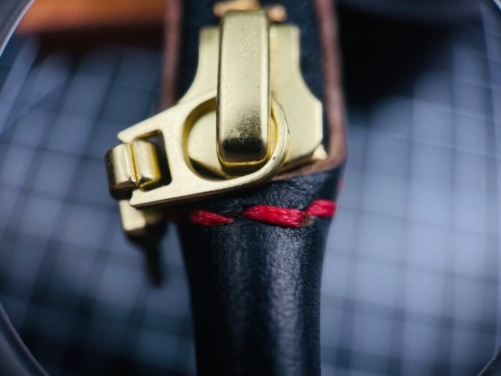 Close-up of a solid brass gold zipper pull on a dark leather bag, showing the depth and weight of authentic luxury hardware construction